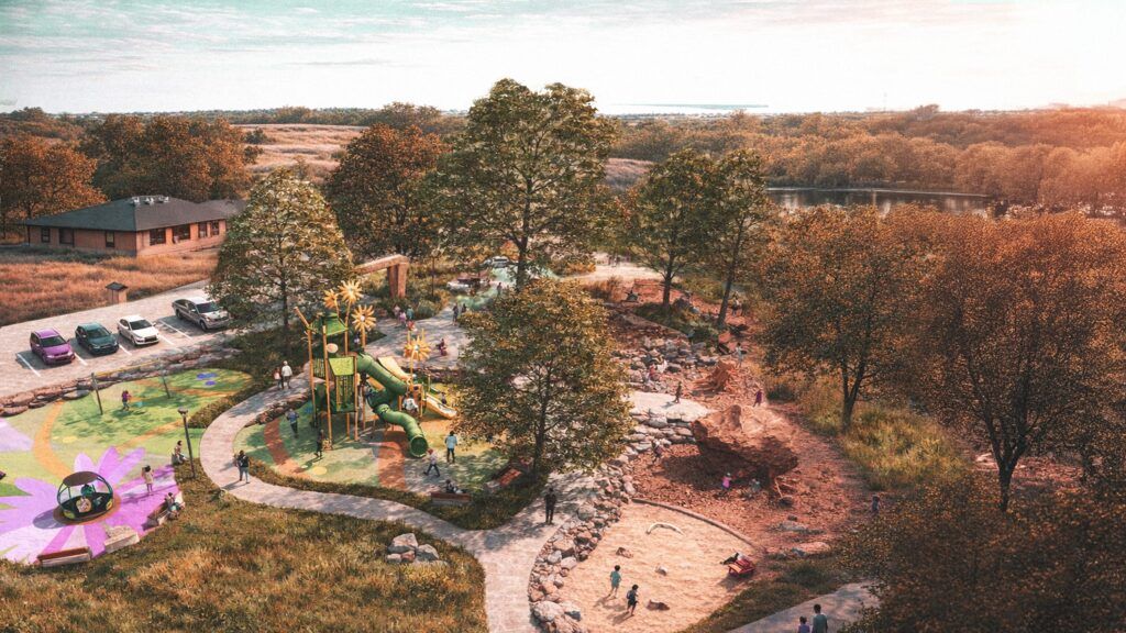 Aerial view of a vibrant playground with slides, climbing structures, sand area, and colorful surfaces surrounded by trees, grassy fields, and parked cars on a sunny day. Children and adults are playing and walking on paths.