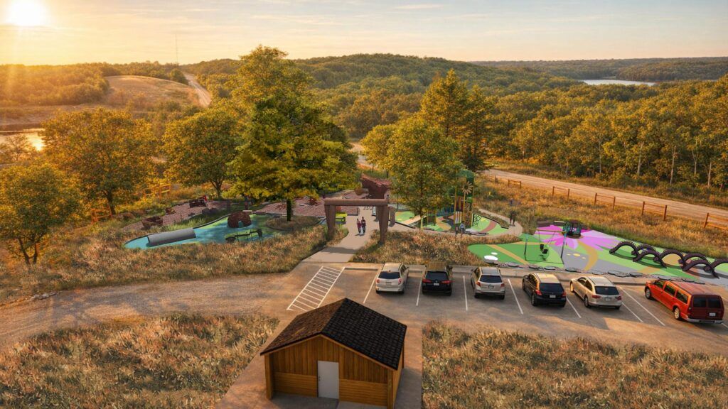 Aerial view of a small parking lot with several cars in front of a wooden shed, leading to a colorful playground surrounded by trees and grassy hills at sunset.